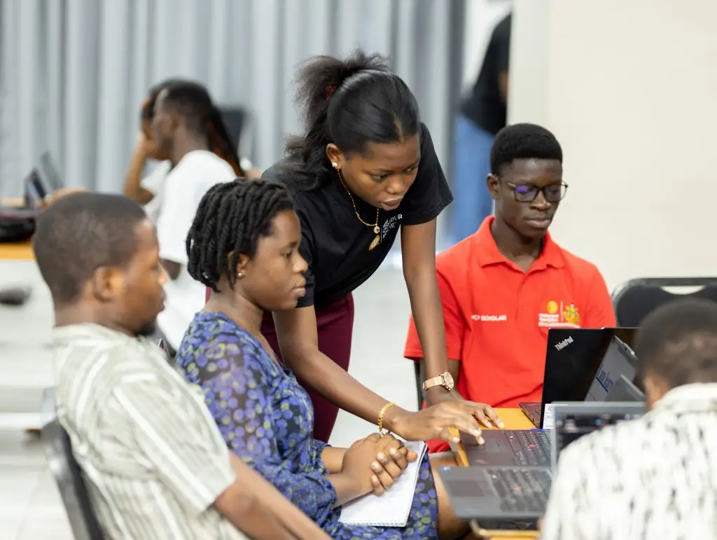 A woman assists participants working on laptops during an indoor training session.