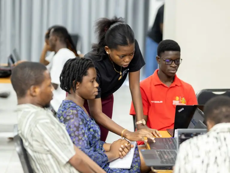 A woman assists participants working on laptops during an indoor training session.