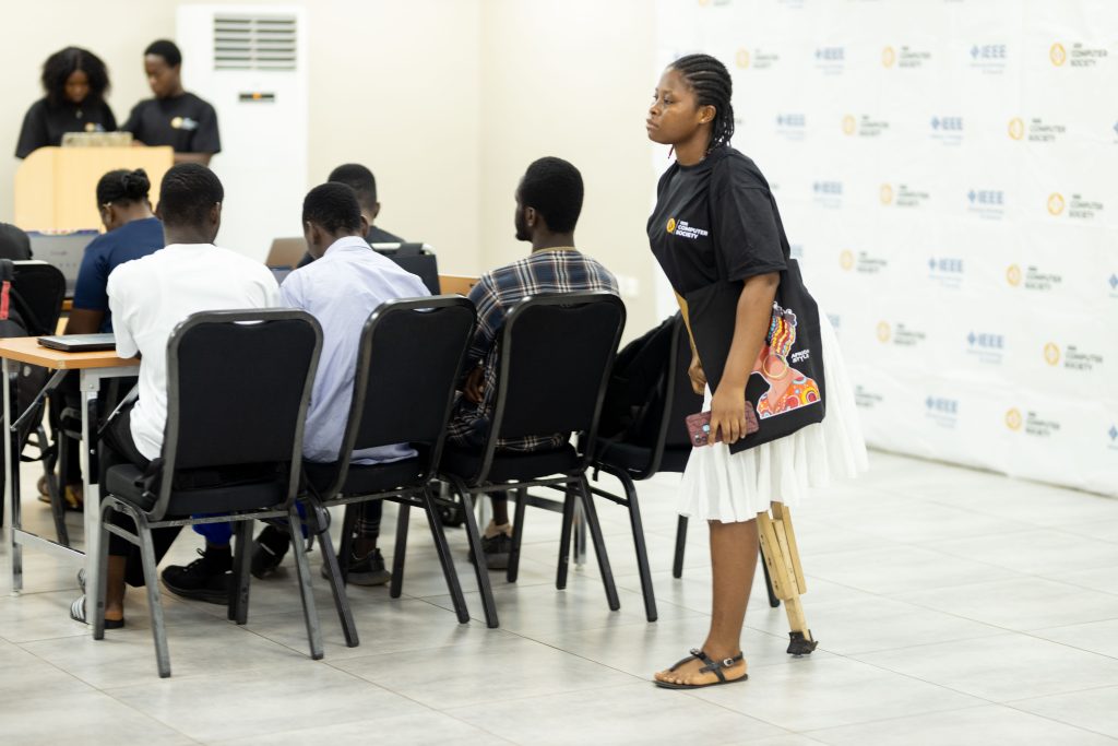 A woman with a prosthetic leg stands near seated participants using laptops at an IEEE Computer Society event.