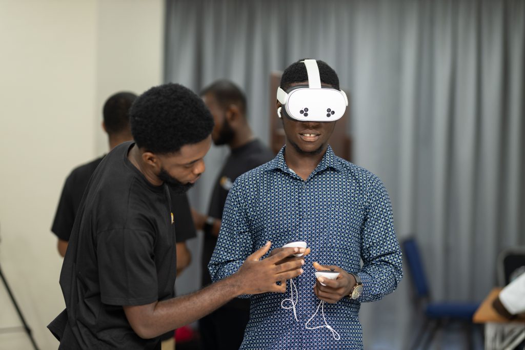 A man wearing a white VR headset and holding controllers is being assisted by another man during a demonstration.