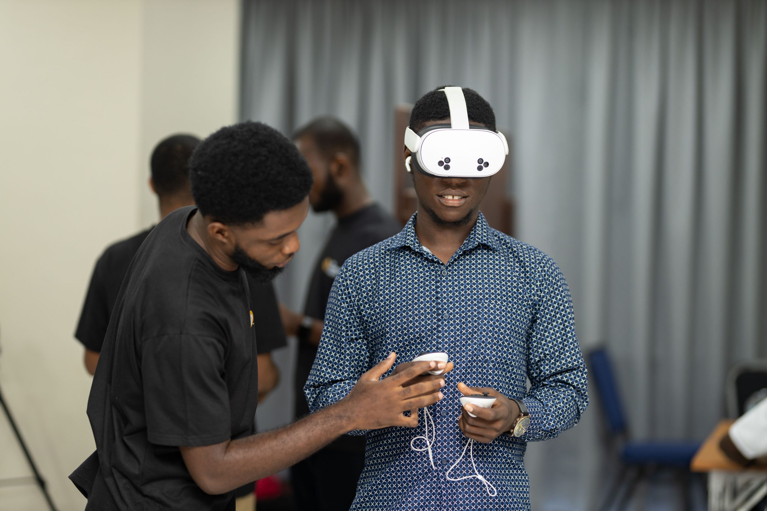A man wearing a white VR headset and holding controllers is being assisted by another man during a demonstration.